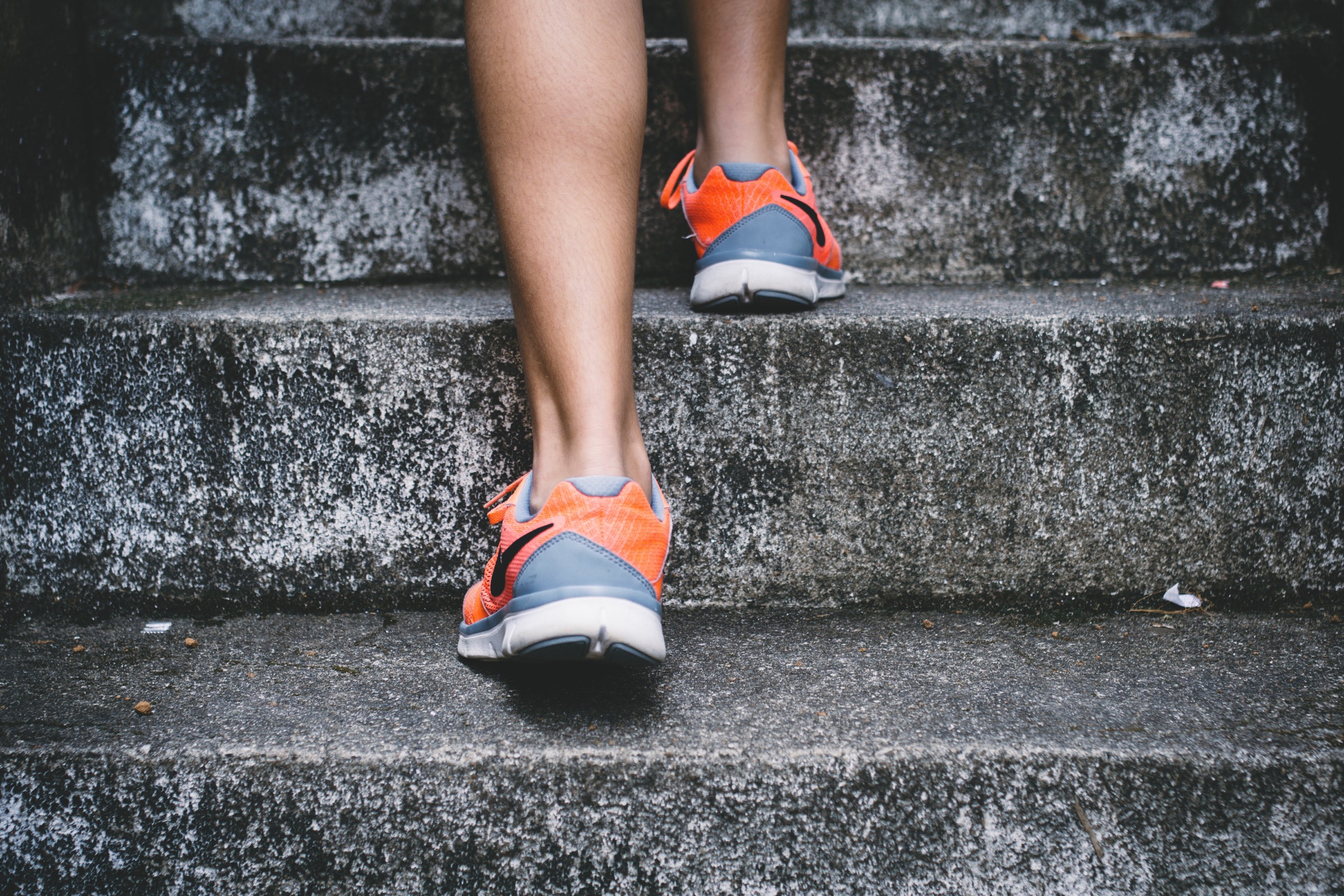 Legs climbing concrete stairs in orange running shoes