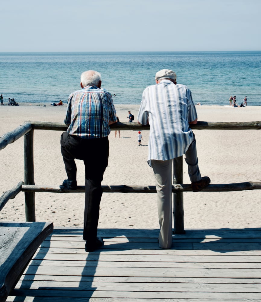 Two older men leaning on a rail by the sea