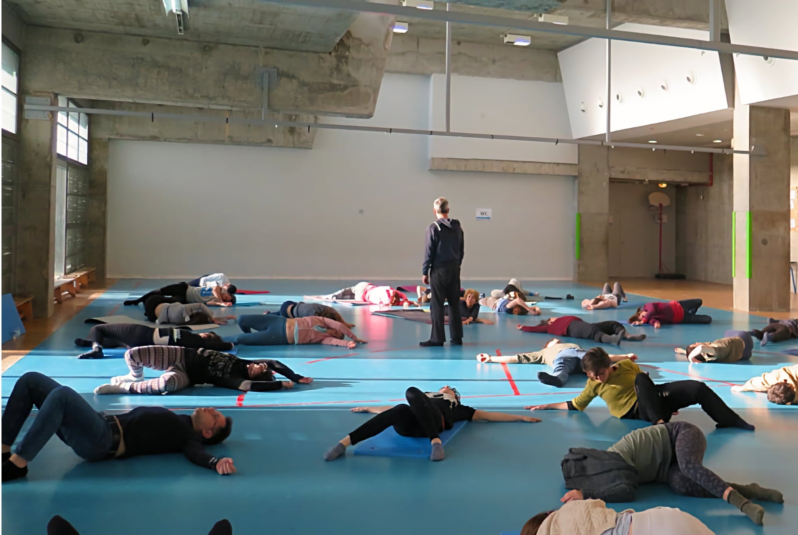 A Feldenkrais group class lying on mats in a gym hall